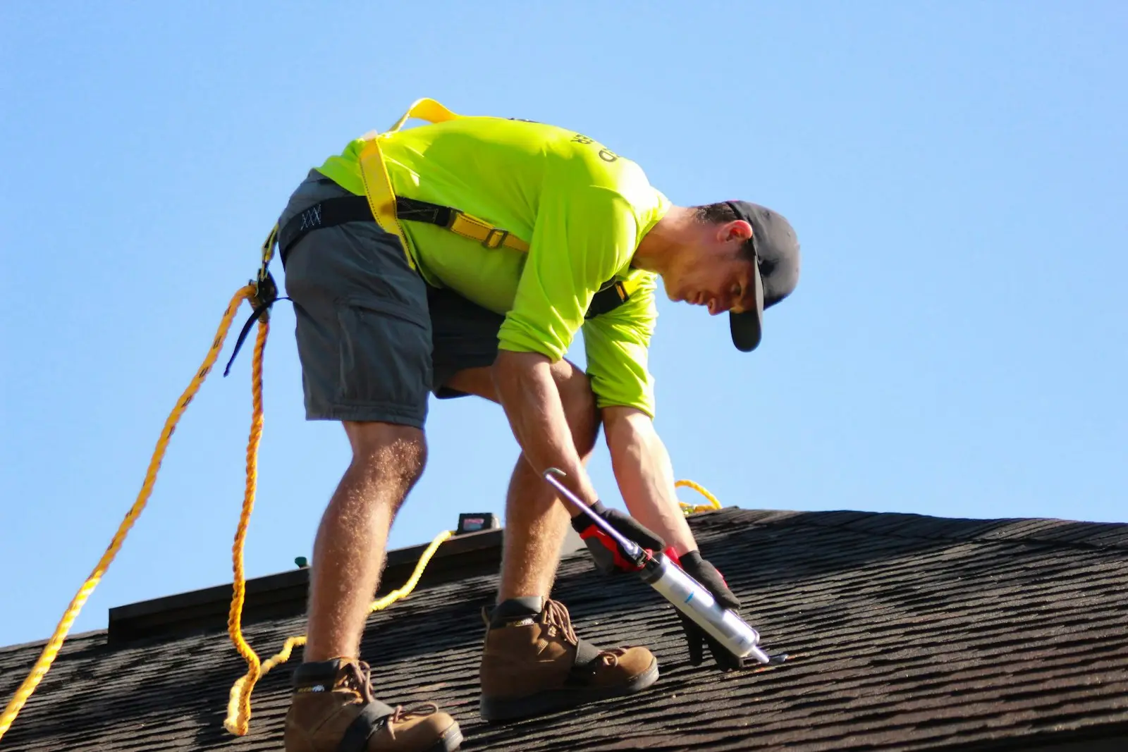 A roofer resealing shingles with a nail gun on a sunny day