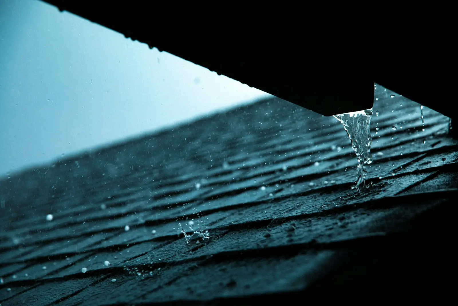 Rain running off a shingle roof edge into the gutter line