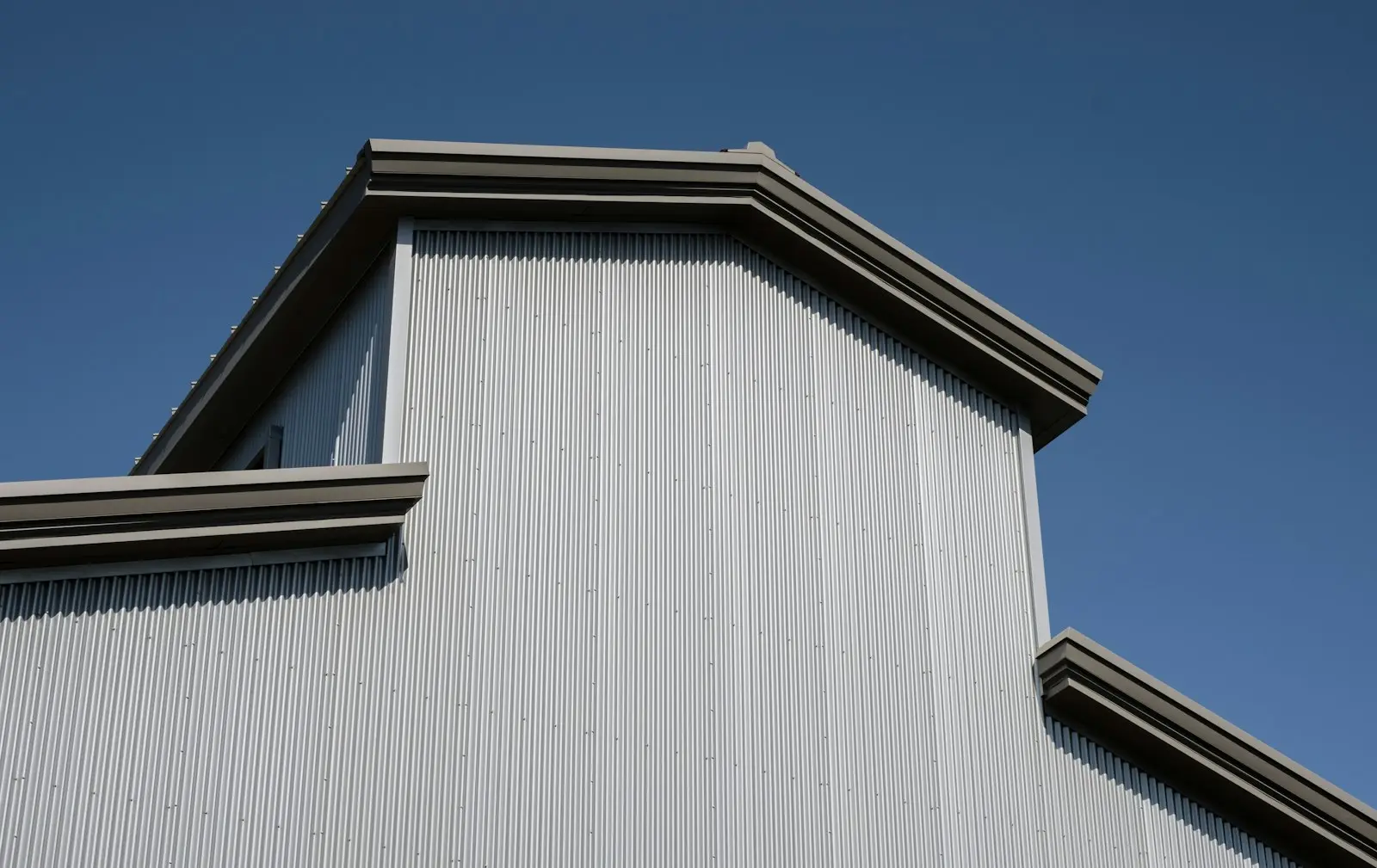 Standing seam metal roof and trim on a clapboard home against a blue sky