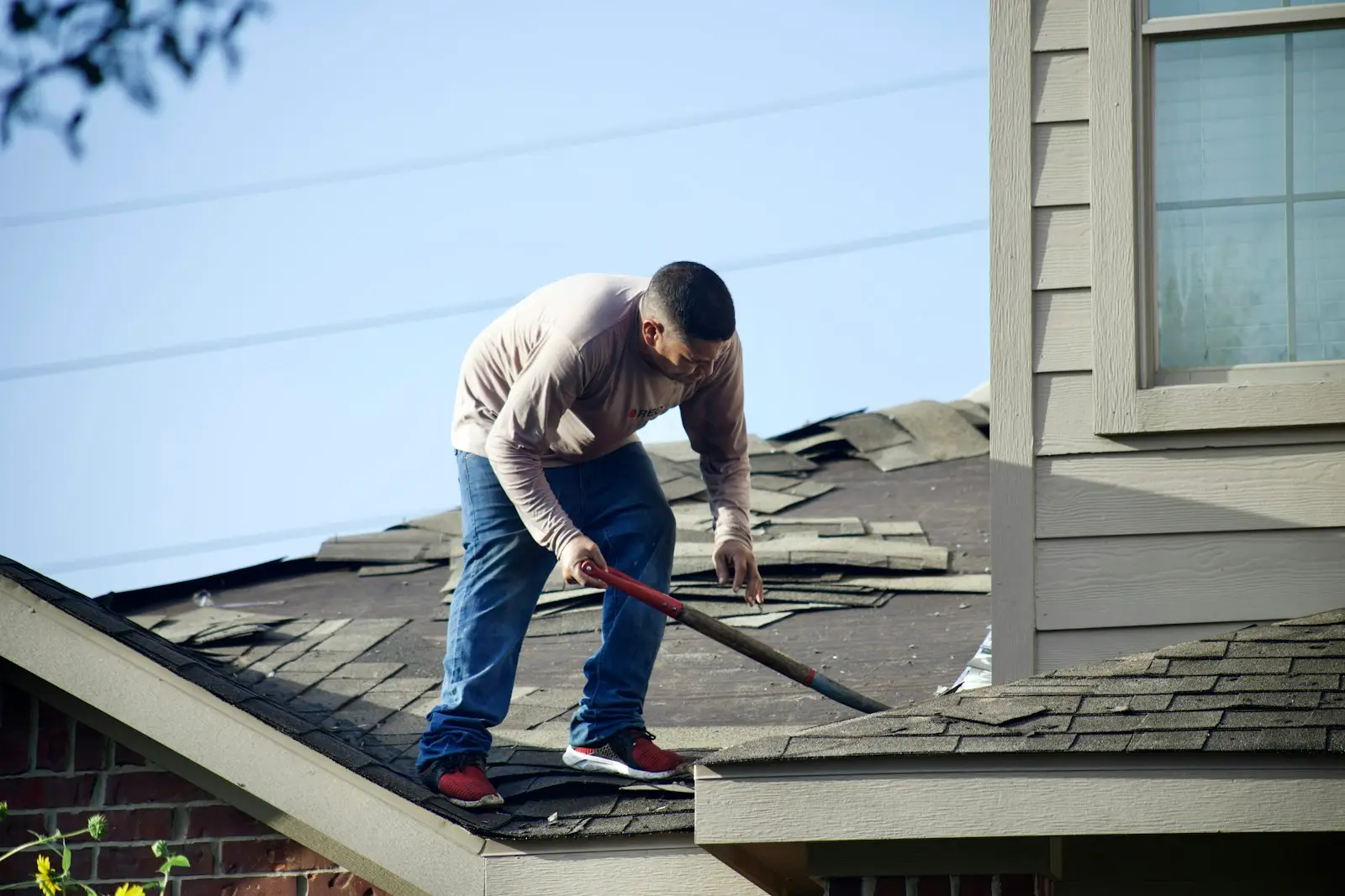 A roofer tearing off storm damaged shingles from a residential roof